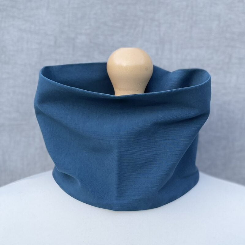 Jersey Neck Gaiter in plain Denim Blue. On a mannequin with pale shoulders and a wooden topper. Light grey background.