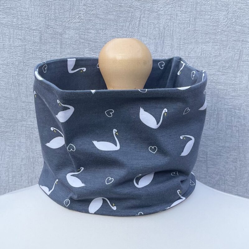 Jersey Neck Gaiter with swans with yellow beaks and black nubs on grey with hearts. On a mannequin with pale shoulders and a wooden topper. Light grey background.